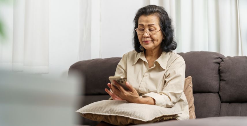 An older woman sitting on a couch, using a cell phone