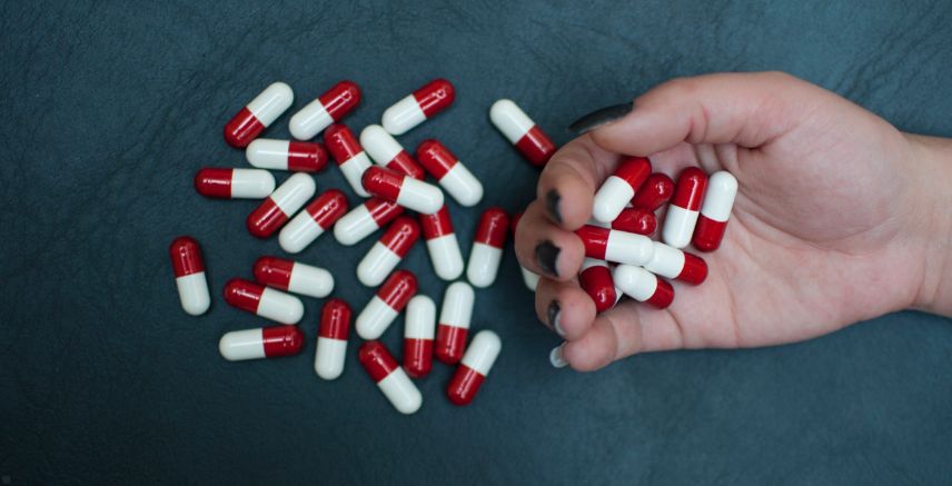 A hand holding red and white pills.